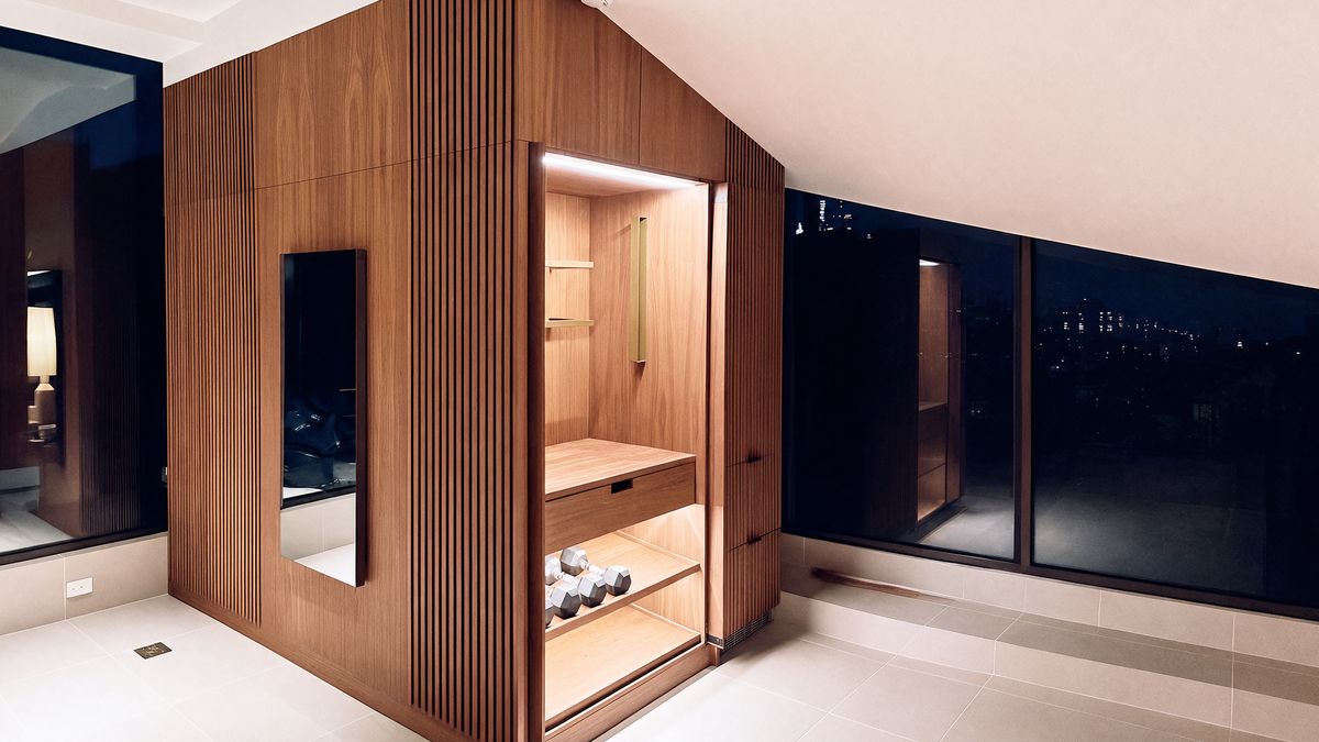 walnut gym volume beside the training screen, open bay lit with dumbbells